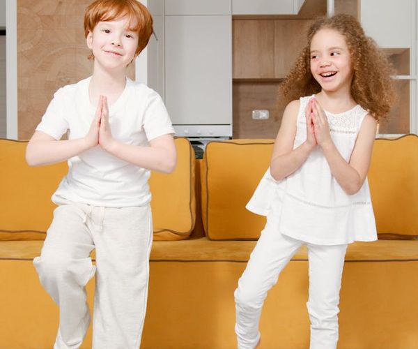 A smiling child balances on one leg in a tree yoga pose.